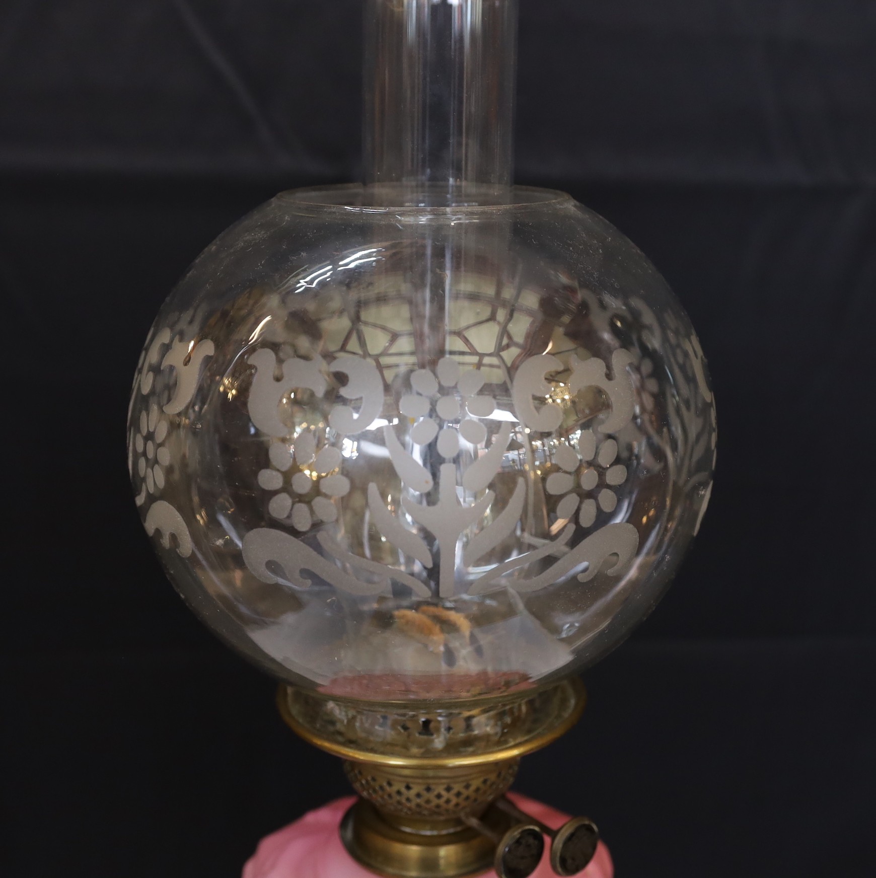 An Edwardian brass Corinthian column oil lamp with opaque pink glass reservoir, etched glass globe and flue, height overall 80cm